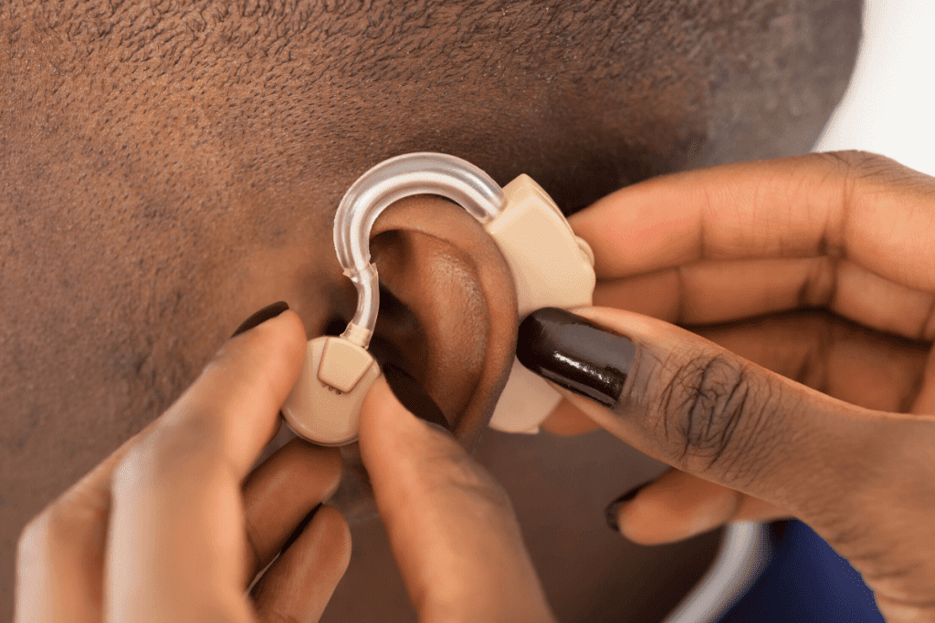 woman's hand putting in a hearing aid in a mans ear